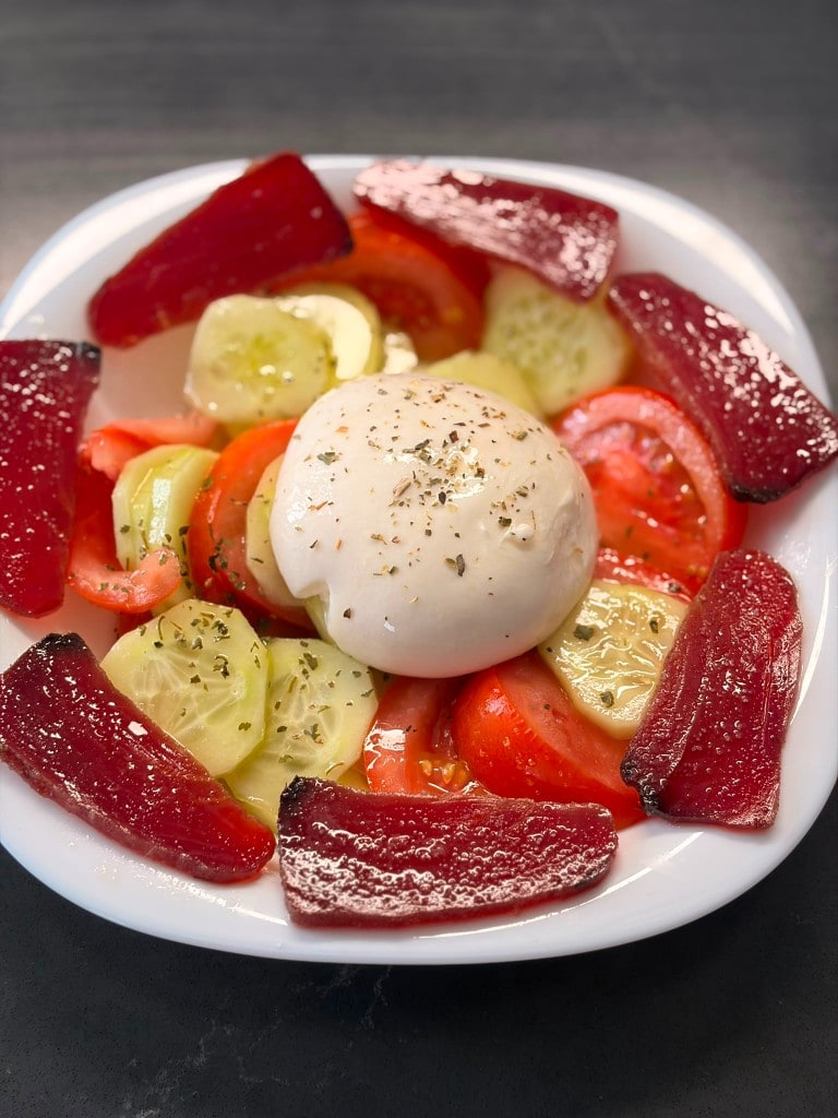 Ensalada de mojama y burrata con tomate y pepino en plato blanco